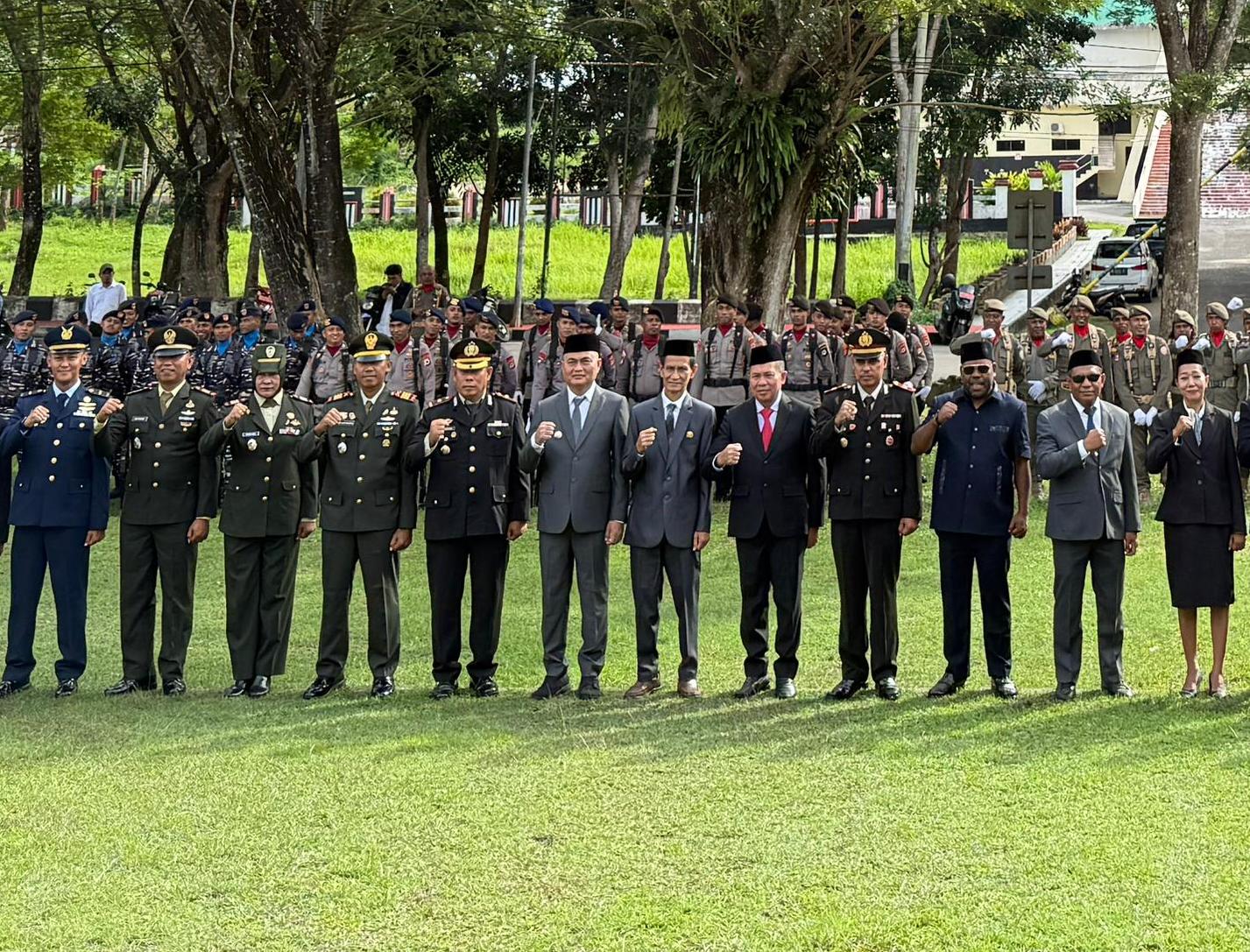 Sejumlah pejabat dan aparat TNI-Polri berdiri tegak di lapangan hijau saat upacara Hari Lahir Pancasila, mengenakan seragam resmi dan jas formal dengan latar pepohonan rindang dan barisan peserta upacara di belakang mereka.