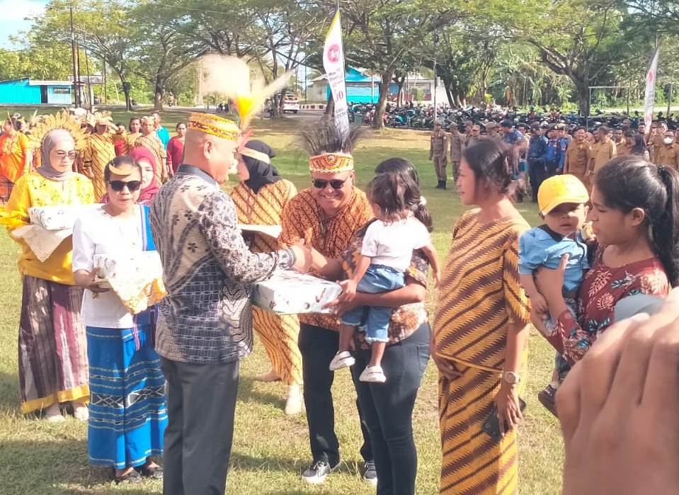 Bupati Kepulauan Aru mengenakan pakaian adat menyerahkan bantuan kepada ibu dan anak dalam kegiatan penanganan stunting di lapangan terbuka, disaksikan oleh masyarakat dan jajaran pemerintah daerah.