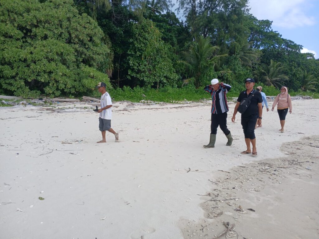 Beberapa tokoh masyarakat berjalan di sepanjang pantai Ujir yang dikelilingi pepohonan hijau dan pasir putih.