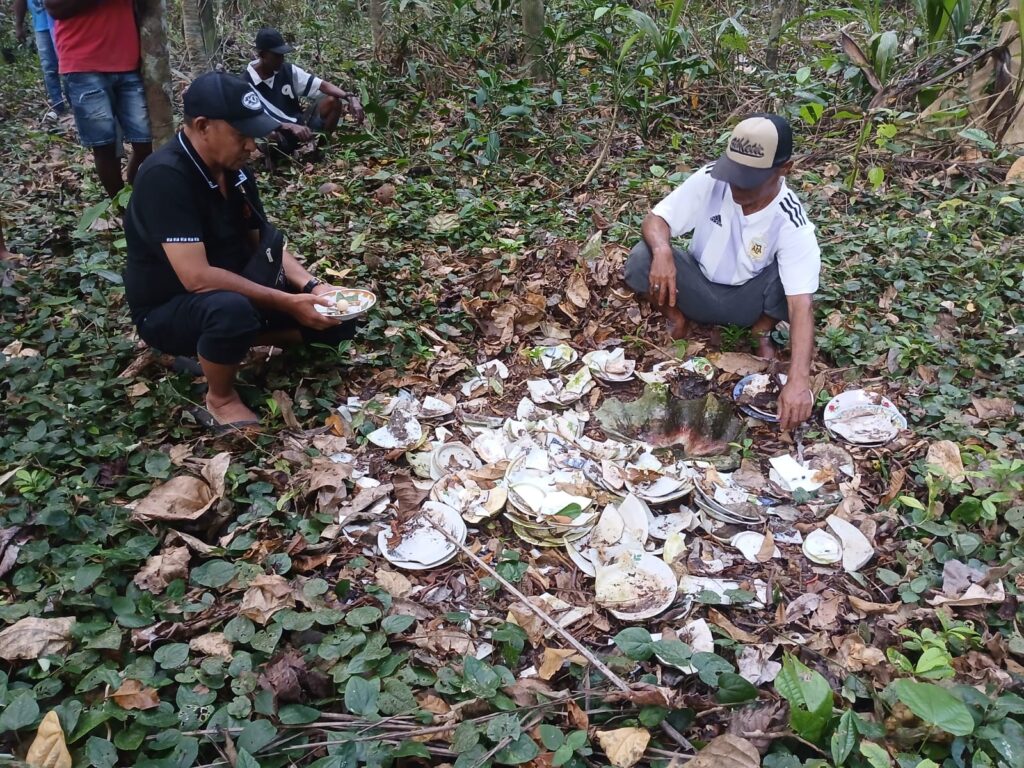 Dua pria memeriksa pecahan piring dan mangkuk kuno yang berserakan di tanah hutan, diduga peninggalan leluhur masyarakat Luang dan Ujir.