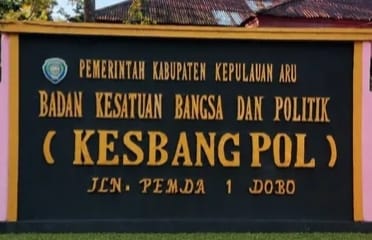 Papan nama Badan Kesatuan Bangsa dan Politik (Kesbangpol) Kabupaten Kepulauan Aru di Jalan Pemda 1 Dobo dengan latar bangunan beratap merah.