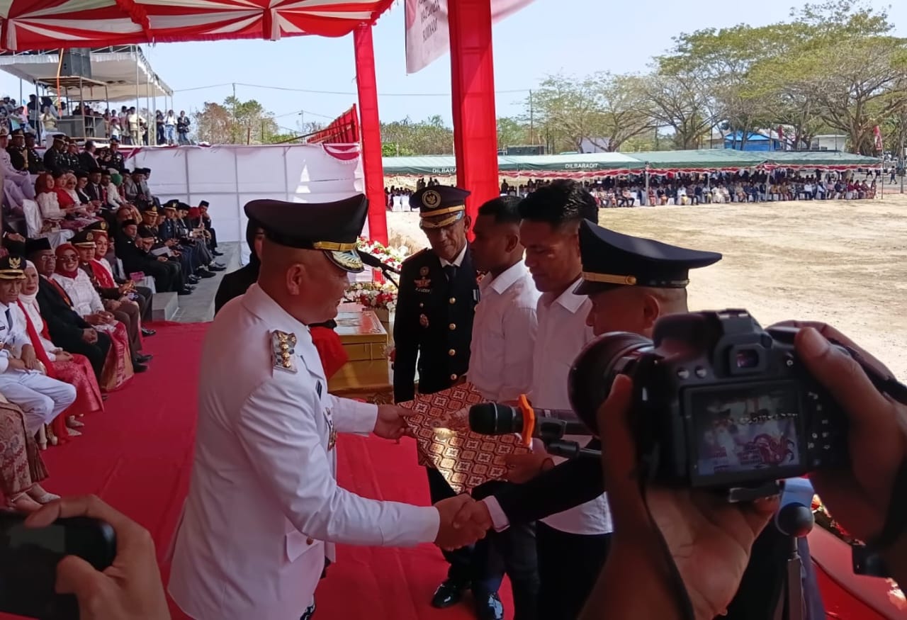 Bupati Kepulauan Aru Timotius Kaidel mengenakan seragam putih upacara menyerahkan dokumen remisi kepada warga binaan di bawah tenda merah putih, disaksikan pejabat dan masyarakat.