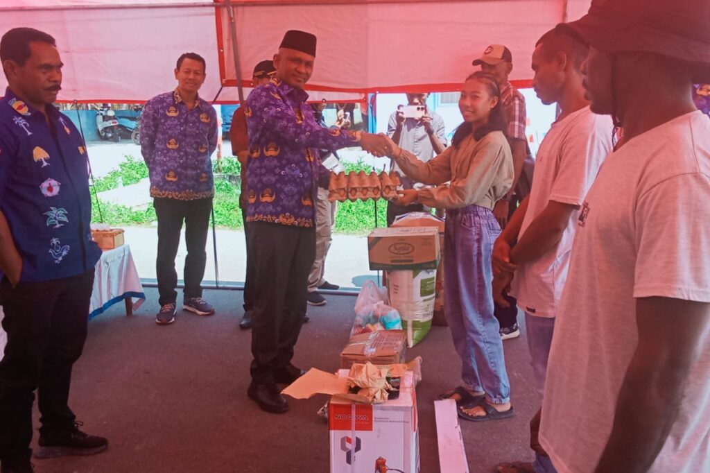 Kadinsos Kepulauan Aru menyerahkan paket bantuan berupa telur kepada penerima manfaat di bawah tenda acara.