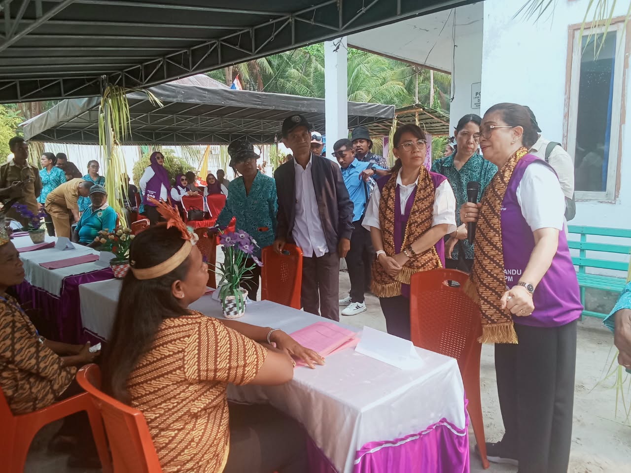 Ketua Tim Pembina Posyandu Maluku mengenakan rompi ungu dan selendang batik berinteraksi dengan kader Posyandu di meja pelayanan Desa Wokam