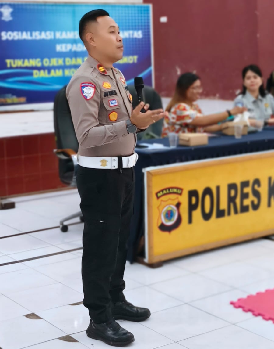 Petugas kepolisian lalu lintas Polres Kepulauan Aru memegang mikrofon menyampaikan materi sosialisasi kepada pengemudi
